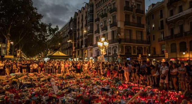 People stand next to candles and flowers placed on the ground, after a terror attack that left many killed and wounded in Barcelona, Spain, Monday, Aug. 21, 2017.
