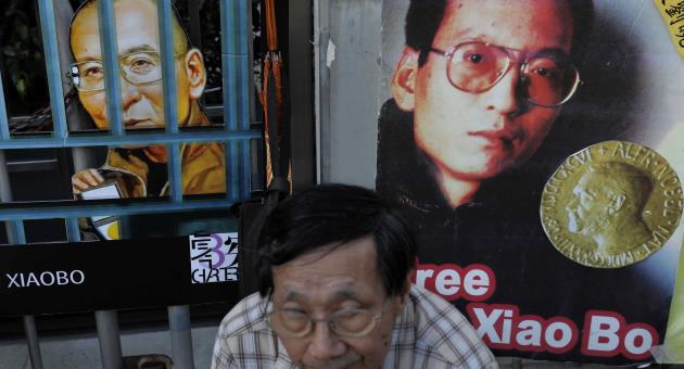 A protester sits in front of pictures of jailed Chinese Nobel Peace laureate Liu Xiaobo during a demonstration outside the Chinese liaison office in Hong Kong, 