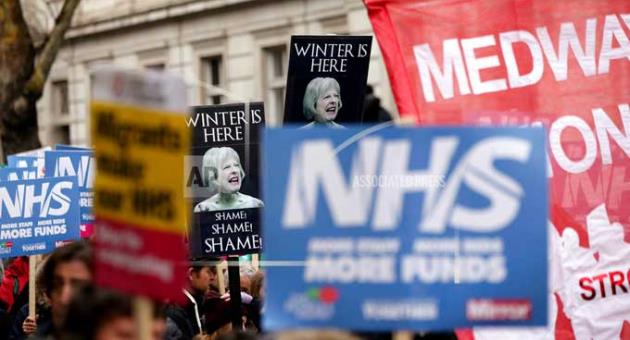 People wave banners depicting Britain's Prime Minister Theresa May, during a protest march in support of the National Health Service (NHS)